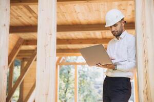Man builder. Foreman with laptop. Contractor for construction company. Architect in unfinished building. Builder in wooden house under construction. Man engineer from construction team photo