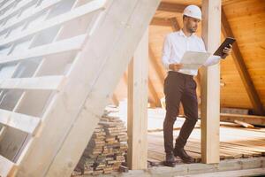 Foreman studies blueprints with tablet. Contractor for construction company. Architect in unfinished building. Builder in wooden house under construction. Man engineer from construction team photo