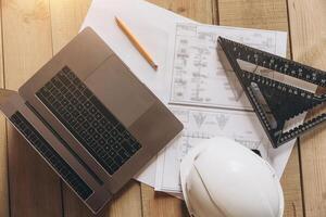 Top view mock -up architectural office desk with copy space, wooden floor with laptop, white helmet construction, pencil, ruler and paper roll, copy space, mock up photo