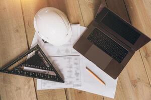 Top view mock -up architectural office desk with copy space, wooden floor with laptop, white helmet construction, pencil, ruler and paper roll, copy space, mock up photo