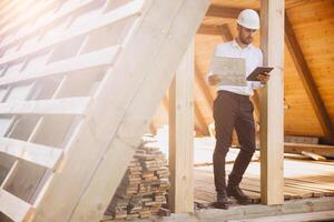 Foreman studies blueprints with tablet. Contractor for construction company. Architect in unfinished building. Builder in wooden house under construction. Man engineer from construction team photo
