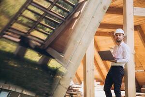 Man builder. Foreman with laptop. Contractor for construction company. Architect in unfinished building. Builder in wooden house under construction. Man engineer from construction team photo