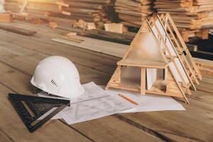 Top view mock -up architectural office desk with copy space, wooden floor with miniature model of house, white helmet construction, pencil, ruler and paper roll, copy space, mock up photo