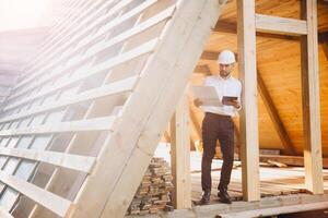 Foreman studies blueprints with tablet. Contractor for construction company. Architect in unfinished building. Builder in wooden house under construction. Man engineer from construction team photo