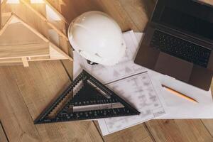Top view mock -up architectural office desk with copy space, wooden floor with laptop, miniature model of house, white helmet construction, pencil, ruler and paper roll, copy space, mock up photo