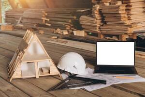 Top view mock -up architectural office desk with copy space, wooden floor with laptop, miniature model of house, white helmet construction, pencil, ruler and paper roll, copy space, mock up photo