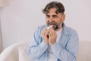 Senior man sneezing into a tissue, experiencing discomfort from cold or allergies, seasonal allergies, virus, flu and sick health, wellness, senior care, and medical treatment for respiratory photo