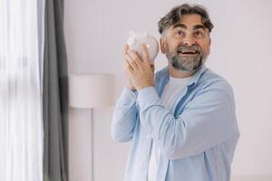 Senior man with a beard shows a white piggy bank suggesting themes of savings, retirement, and financial planning with copy space photo