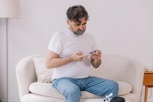 Diabetic senior man on wheelchair checking blood sugar level with fingerstick testing glucose meter. Elderly man with type 1 diabetes using blood glucose monitor at home. photo