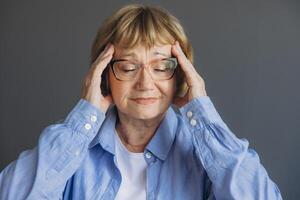 Portrait of senior woman at home with a headache, feeling pain and with an expression of being unwell on gray background photo