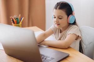 Smiling little girl in headphones watch lesson on computer with alphabet, happy little child in earphones have online web class using laptop at home, home schooling concept photo