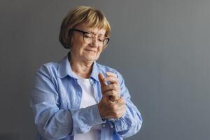 Elderly woman suffering from pain in hand, close up on gray background photo