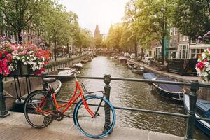Old bicycle on the bridge in Amsterdam, Netherlands against a canal during summer sunny day. Postcard iconic view. Tourism concept. photo