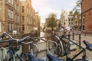 Old bicycle on the bridge in Amsterdam, Netherlands against a canal during summer sunny day. Postcard iconic view. Tourism concept. photo