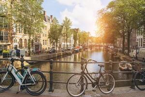 Old bicycle on the bridge in Amsterdam, Netherlands against a canal during summer sunny day. Postcard iconic view. Tourism concept. photo