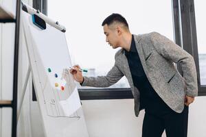 Asian businessman standing writing diagram and graph on whiteboard with presentation to manager in office room. photo