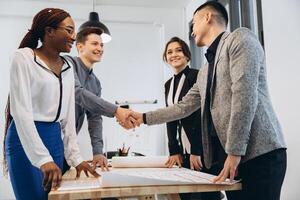 Diverse businessmen shaking hands after signing contracts at group multiracial meeting, african, caucasian and asian partners in suits handshaking promising good deal after successful negotiations photo