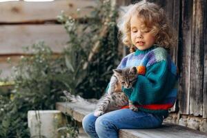 Portrait of a beautiful and happy curly girl in a knitted sweater playing with a kitten near a wooden wall photo