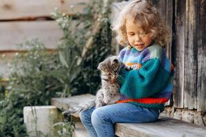 Portrait of a beautiful and happy curly girl in a knitted sweater playing with a kitten near a wooden wall photo
