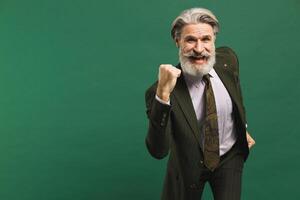 A middle-aged bearded man in a khaki suit screams loudly and holds his fist of happiness against a green background. Stock and win concept photo