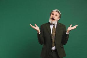 Bearded middle-aged man in khaki suit waving his hands to the side on a green background with copy space. photo