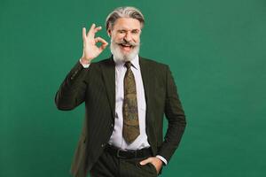 Bearded middle-aged man in khaki suit shows okay on green background with copy space. photo