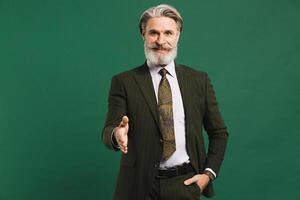 Middle-aged bearded man in khaki suit hand greetings on green background photo