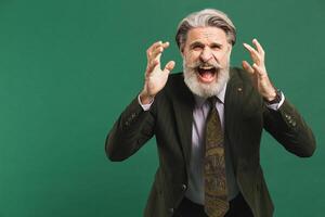 A middle-aged bearded man in a khaki suit shouts loudly and holds his fists against on a green background photo