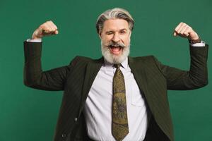Bearded middle-aged man in khaki suit shows biceps and smiles emotionally on green background photo