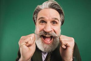 A middle-aged bearded man in a khaki suit shouts loudly and holds his fists against on a green background photo