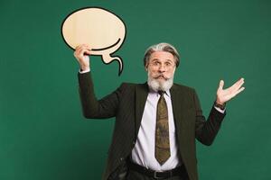 Business middle-aged bearded man in khaki suit holding emoji with copy space and waving a hand that does not know on a green background photo