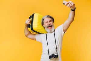 Stylish bearded and mustachioed man smiling and taking a selfie on his smartphone with a yellow suitcase. photo