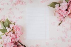 Sprigs of the sakura tree with flowers and petals around blank of paper on trendy marble background. Place for text. The concept of spring came. Top view. Flat lay photo
