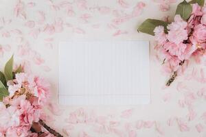 Sprigs of the sakura tree with flowers and petals around blank of paper on trendy marble background. Place for text. The concept of spring came. Top view. Flat lay photo