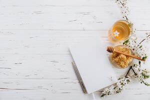 Spring composition. A cup of herbal tea, a jar of honey and cherry blossom near notebook on a white wooden background, top view. Place for text. Healthy food planning concept. photo