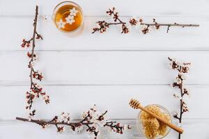 Spring composition. Frame with cup of herbal tea, a jar of honey and cherry flowers, top view. Healthy food concept photo