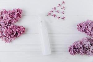 Freshener and floral scent concept. White bottle of perfume with spray of lilac flowers on pink background, flat lay and top view photo