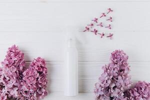 Freshener and floral scent concept. White bottle of perfume with spray of lilac flowers on pink background, flat lay and top view photo
