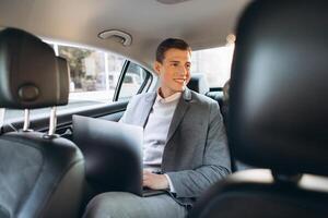 A modern businessman using a laptop computer while sitting in the back seat of a car. photo