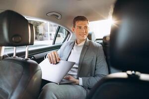 A modern businessman using a laptop computer while sitting in the back seat of a car. photo