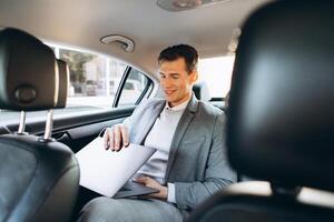 A modern businessman using a laptop computer while sitting in the back seat of a car. photo