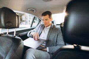 A modern businessman using a laptop computer while sitting in the back seat of a car. photo