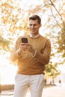 Modern handsome smiling man in yellow and white clothes talking on the phone in the park at sunset photo
