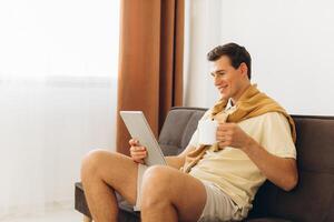 Handsome young man in yellow casual clothes sitting at home reading books and drinking coffee photo