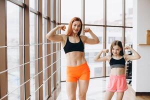 Beautiful strong woman and charming little daughter are showing their biceps and smiling while working out at gym photo
