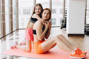Happy smiling mother and daughter sitting and hugging on the floor in the gym photo