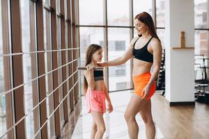 Mom and Daughter are doing exercises. Family in a gym. Little girl with strong mother are training with dumbbells photo