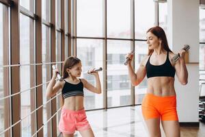 Mom and Daughter are doing exercises. Family in a gym. Little girl with strong mother are training with dumbbells photo