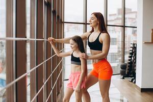 Strong mother and her child daughter are standing and looking the window in the gym photo