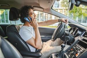 Man with curly hair driving a car, smoking a cigarette and using phone photo